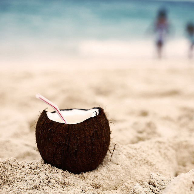 Noix de coco fendue sur la plage, avec une paille.