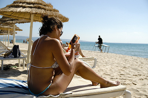 Une femme en maillot de bain bronze sur la plage et se met de l'huile protectrice.