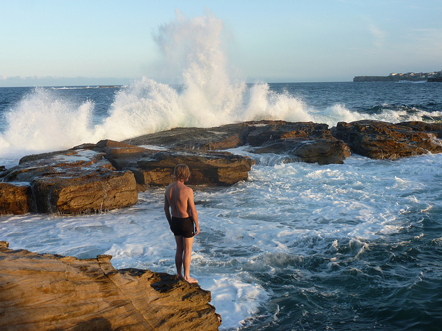 Personne face aux vagues qui se brisent sur des rochers.