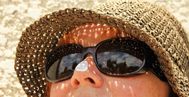 Femme avec lunettes de soleil, chapeau et crème solaire sur le nez.