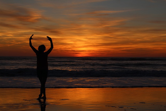 Photographie d'un coucher de soleil avec une personne qui danse sur la plage.