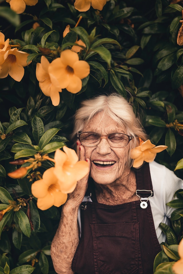 Vieille femme qui sourit dans des fleurs.